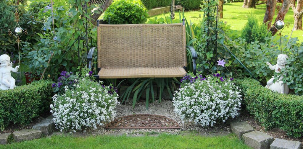  Eine gemütliche Gartenbank umgeben von üppigem Grün und blühenden Blumen, eingerahmt von Hecken und Statuen, bietet einen einladenden Platz zum Verweilen und Entspannen im Garten.