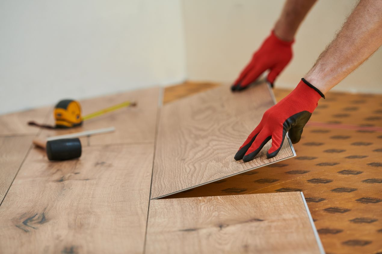 Handwerker verlegt Holzoptik-Vinylboden mit integrierter Trittschalldämmung, mit Werkzeugen im Hintergrund.